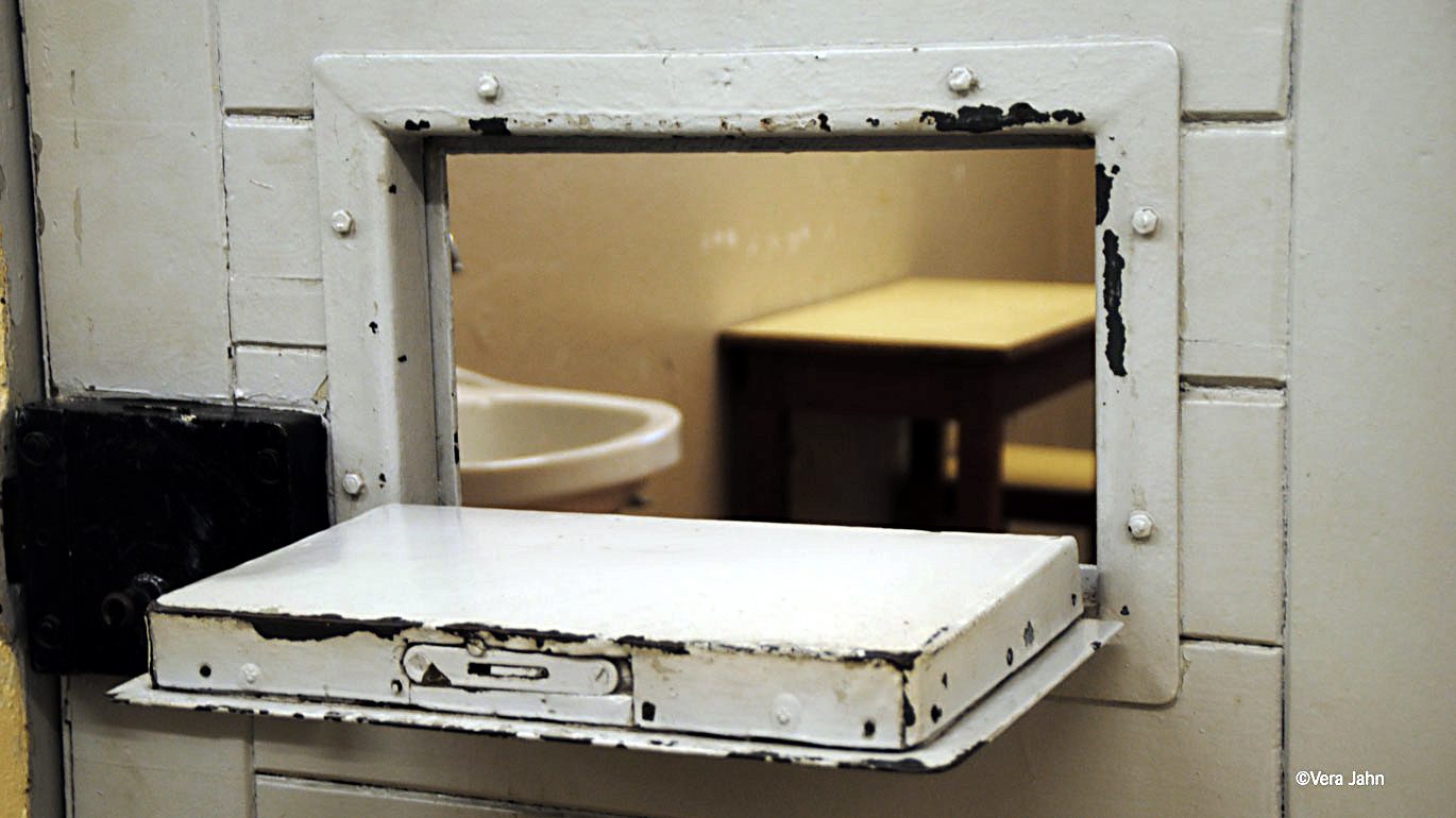 Die geöffnete Klappe einer Gefängnistür zeigt den Blick eine Zelle. .
